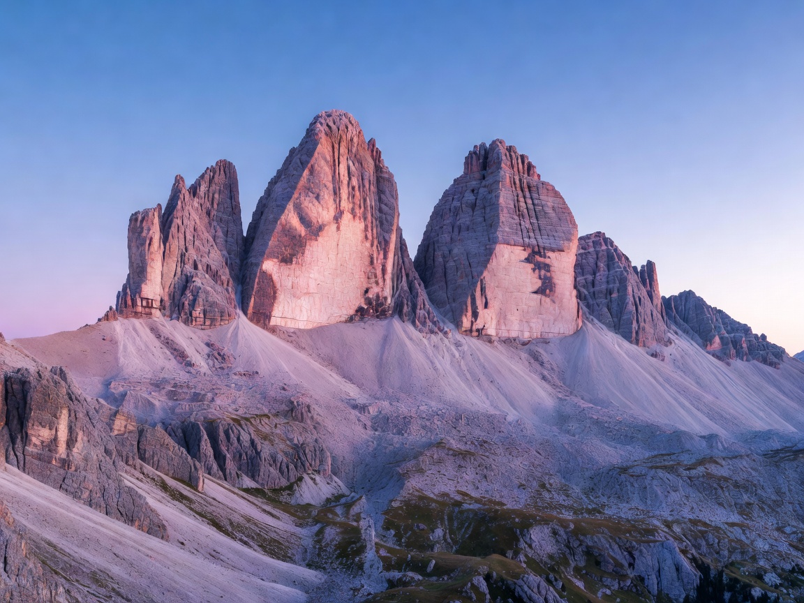 Alpenglow pink light hitting jagged peaks of Tre Cime di Lavaredo in Dolomites